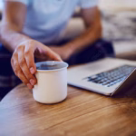 Close up of man taking mug with morning coffee. Man is dressed in pajamas and is easily tracking his net worth as learned on Think and Talk Money.